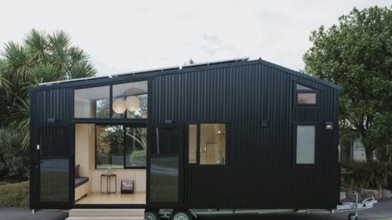 The First Light tiny home is sided with black corrugated steel and features expansive windows and French doors that connect the plywood interior to the outdoors.