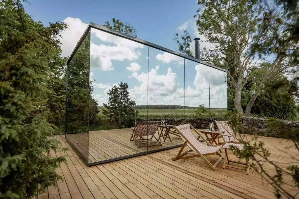 A sleek ÖÖD House prefab home with a mirrored exterior blending into its surroundings.